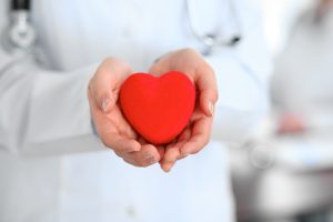 Female,Doctor,With,Stethoscope,Holding,Heart.,Patients,Couple,Sitting,In