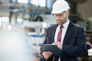 Mid,Adult,Businessman,Writing,On,Clipboard,In,Metal,Industry