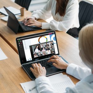 Digital conference. Online presentation. Virtual meeting. Female employee using laptop working with business team discussing statistics report on screen with charts graphs.