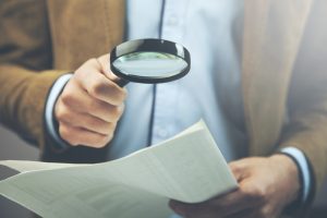 Businessman,Hand,Document,And,Magnifier,In,Office