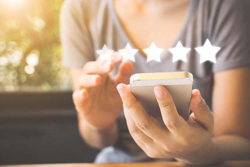 A woman holding a mobile phone with 5 starts above the phone