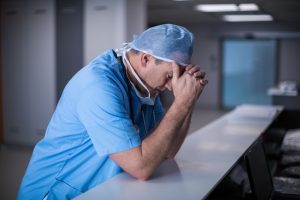 Depressed,Surgeon,Leaning,On,Desk,At,Hospital.,Healthcare,Workers,In