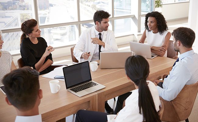 Group Of Medical Staff Meeting Around Table In Hospital