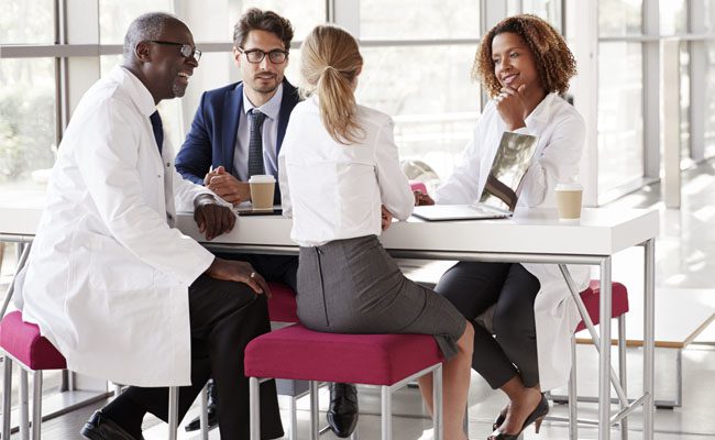 Four doctors talking at a table in a modern hospital lobby