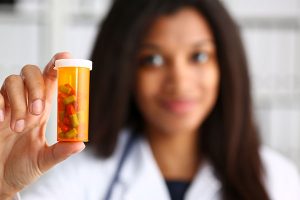 Female black doctor hands hold jar of pills closeup. 