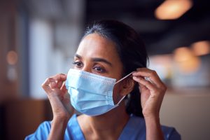 Female,Doctor,In,Scrubs,Putting,On,Face,Mask,Under,Pressure