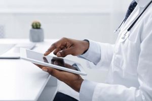 Technologies in medical field. Cropped of black doctor using digital tablet at workplace