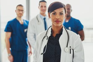 Confident,Female,Doctor,In,Front,Of,Team,,Looking,At,Camera