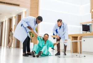 Group of people help female patient falling on the ground in hospital. Attractive African American women having an accident after doing physical therapy then rescued by doctor in corridor of clinic.