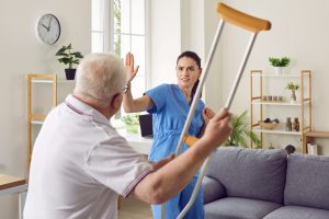 male-patient-swinging-crutch-at-female-nurse