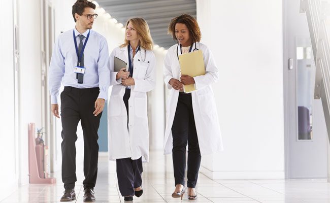 Three young male and female doctors walking in hospital