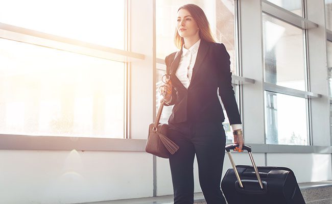 Pretty smiling female flight attendant carrying baggage going to airplane in the airport.