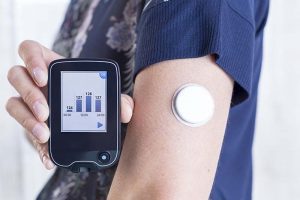 closeup of a hand of a young woman showing a reader after scanning the sensor of the glucose monitoring system beside the sensor placed on her arm - focus on the reader