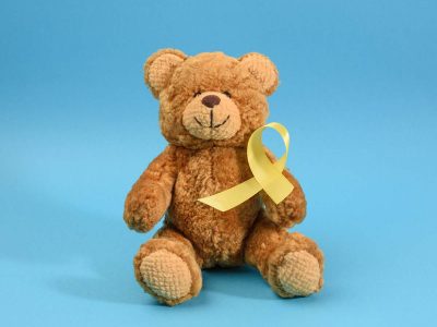 brown teddy bear holds in his paw a yellow ribbon folded in a loop on a blue background