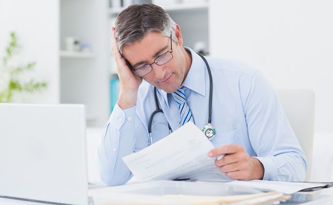 Tensed male doctor reading document at table in clinic